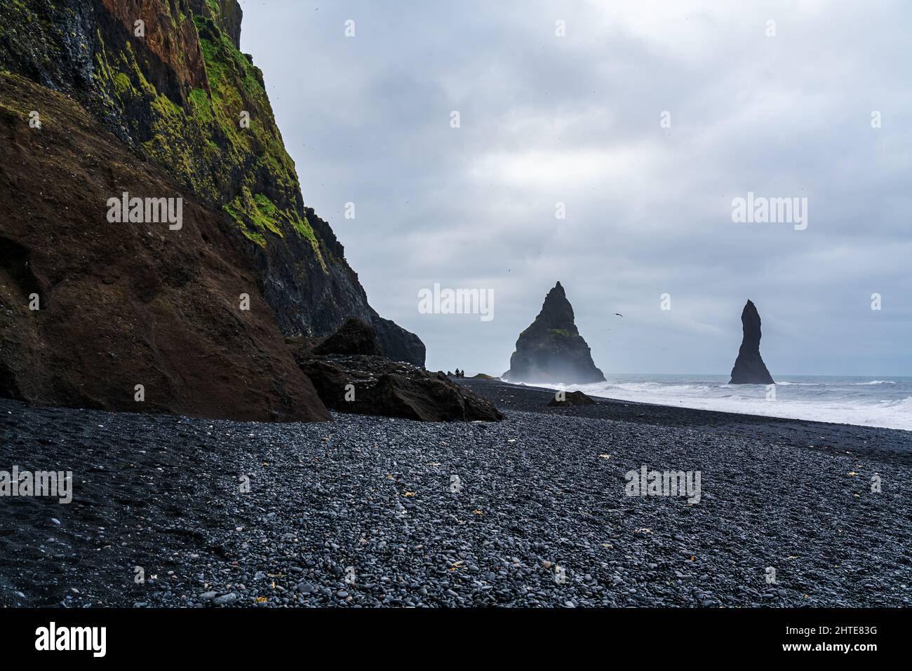 Paesaggio vulcanico della spiaggia di sabbia nera di Reynisfjara al monte Reynisfjall con una coppia a piedi e le onde tempestose dell'Oceano Atlantico. Foto Stock