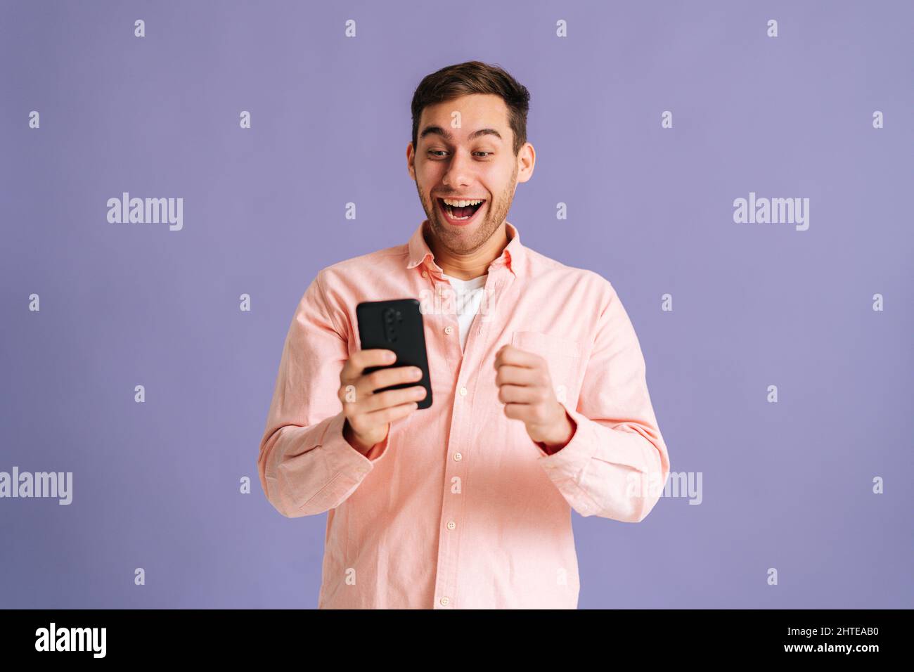 Ritratto di sorpreso eccitato giovane uomo urlando durante l'uso del telefono cellulare appena scoperto grande grande vittoria notizie, facendo il gesto del vincitore dire sì. Foto Stock