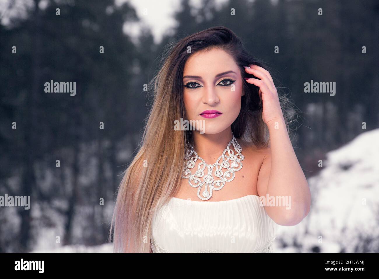 Donna rumena elegante in un abito bianco che guarda la fotocamera contro uno sfondo sfocato inverno Foto Stock