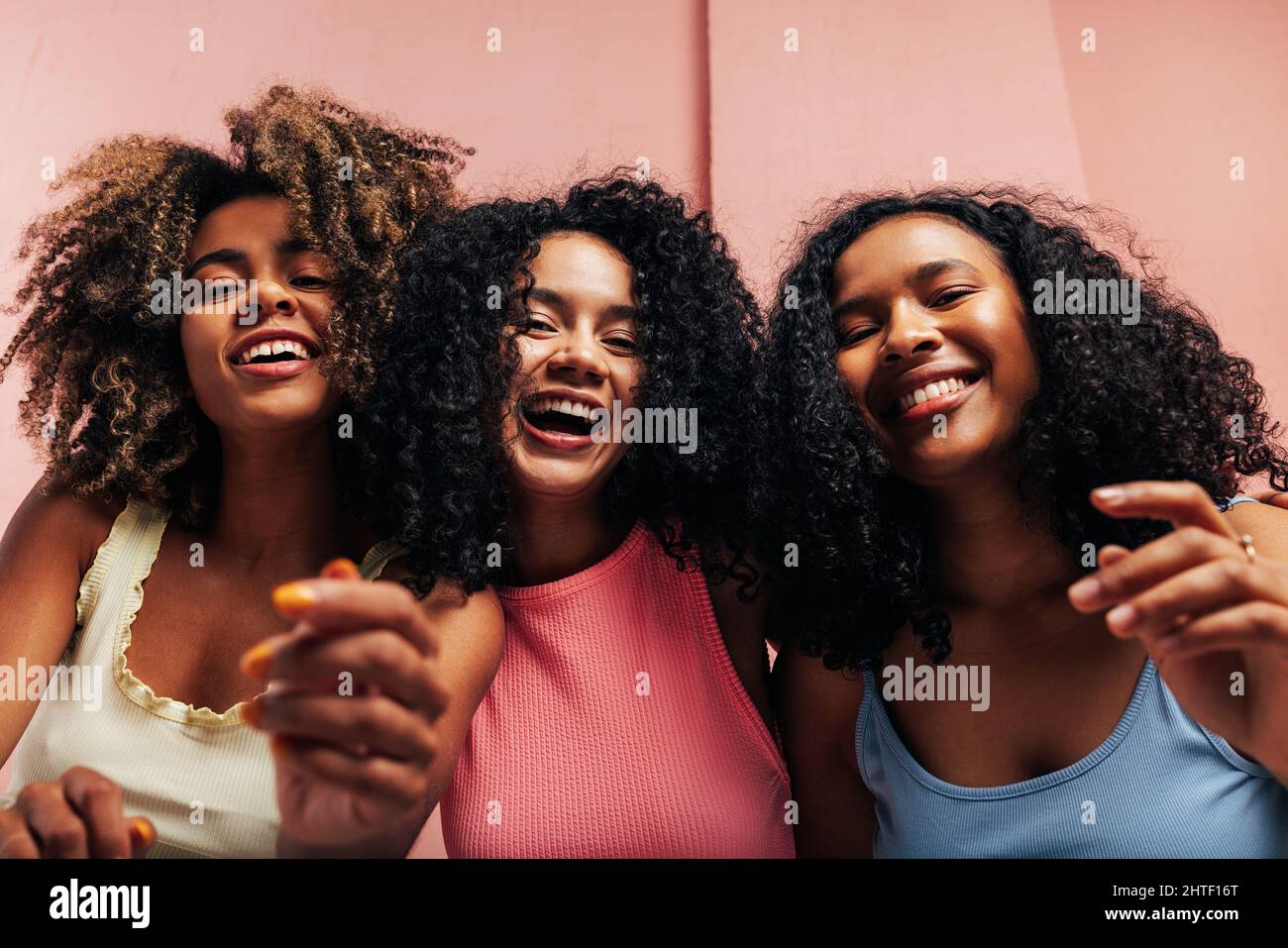 Tre amiche felici con capelli ricci che ridono insieme e guardano la fotocamera Foto Stock