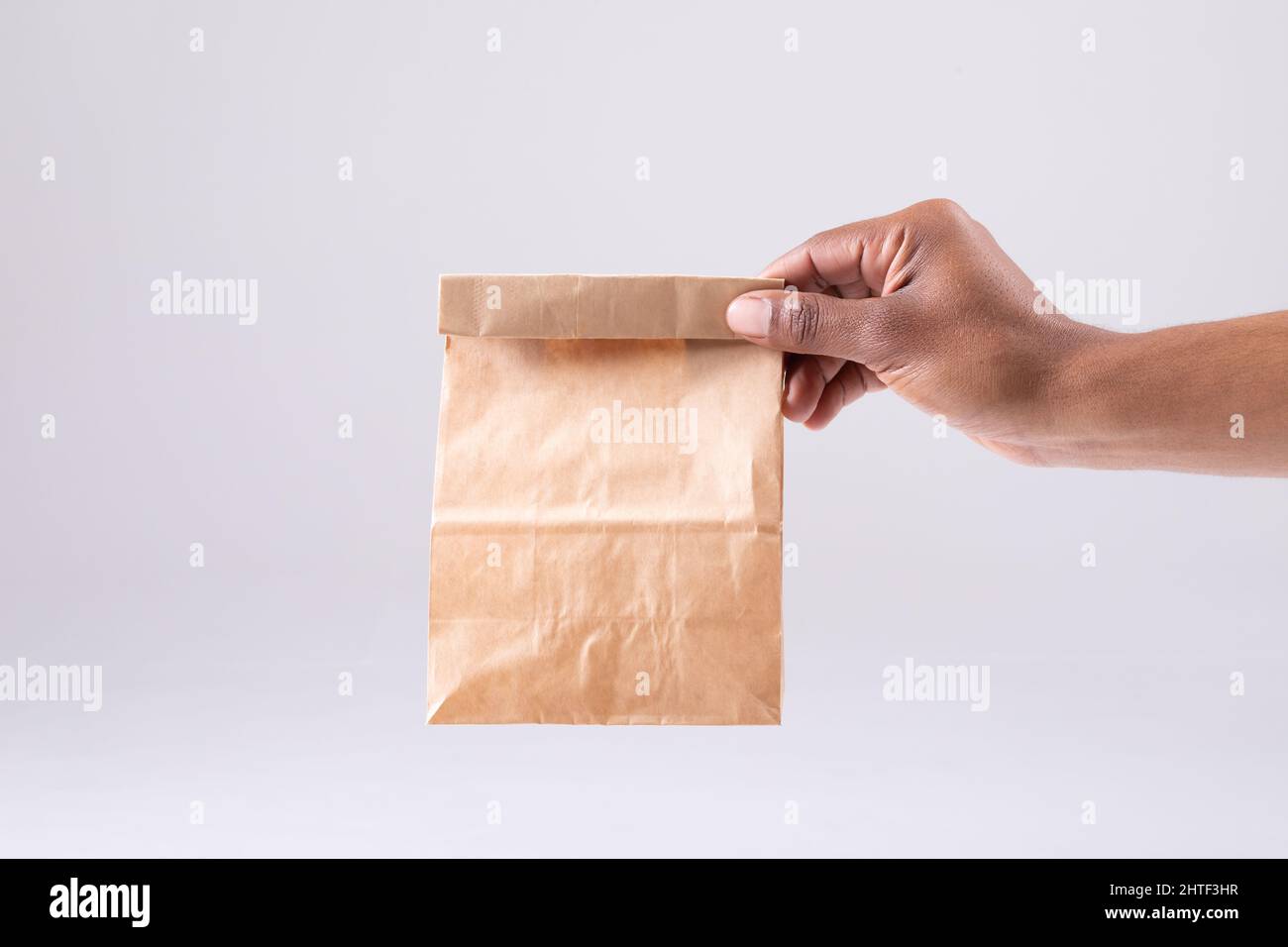 Immagine ritagliata della persona afroamericana che tiene a mano la borsa da pranzo di carta su sfondo bianco Foto Stock
