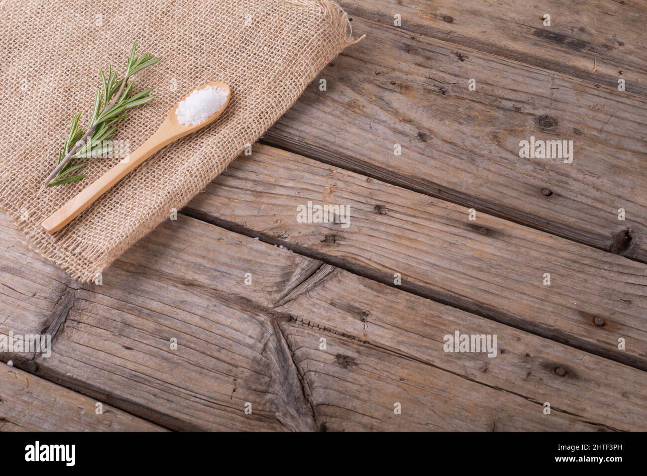 Alto angolo di vista del sale di roccia in cucchiaio di legno e rosmarino su tessuto di iuta al tavolo con spazio vuoto Foto Stock