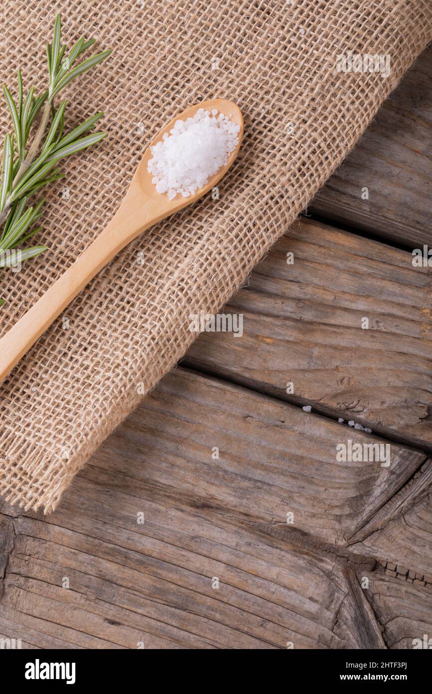 Primo piano di sale bianco di roccia in cucchiaio di legno di rosmarino su tessuto di iuta a tavola Foto Stock