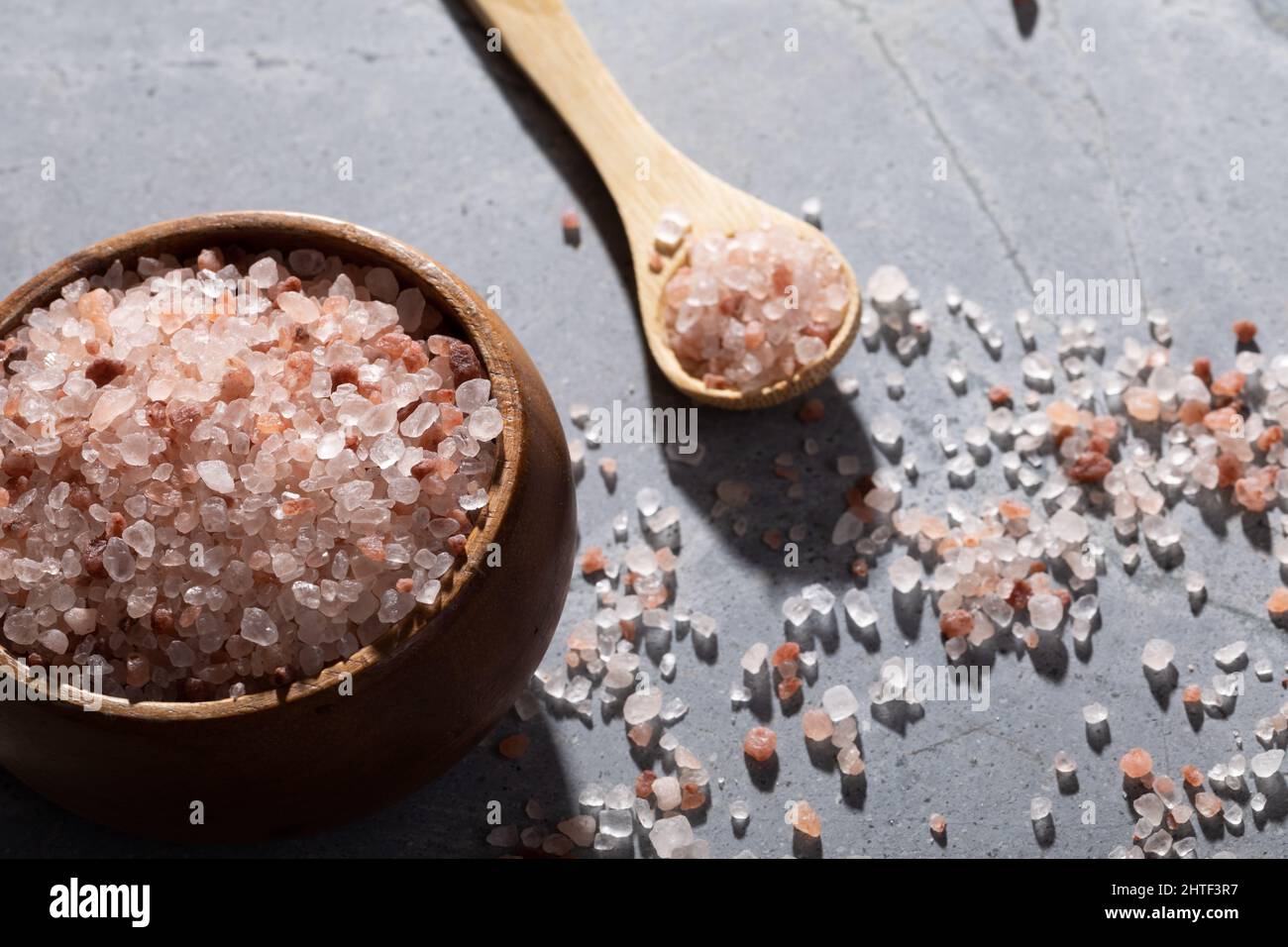 Caduta leggera su sale di roccia rosa in una ciotola di legno e cucchiaio sul tavolo Foto Stock