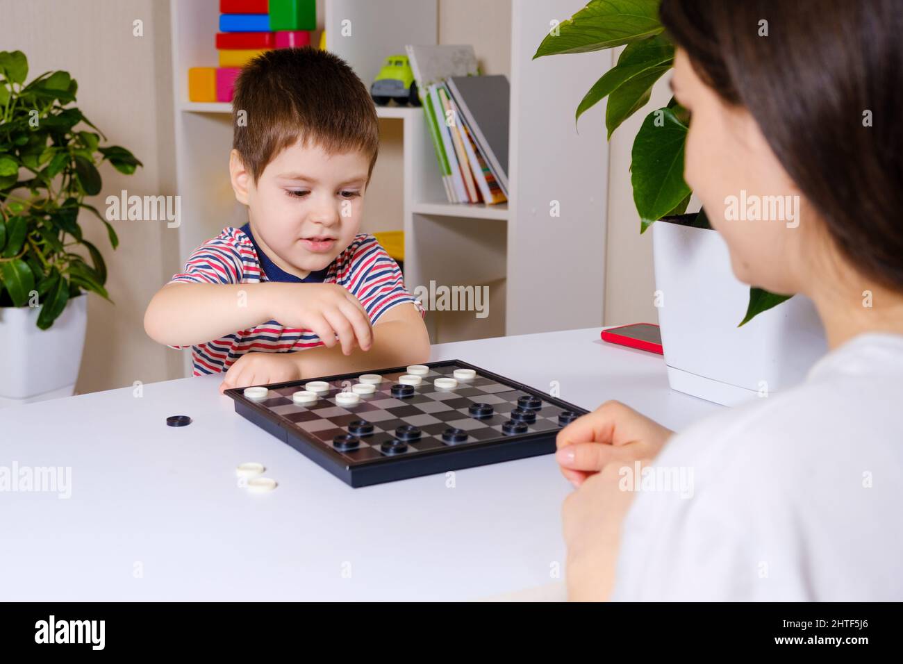 Madre e figlio giocano a dama in casa. Giochi da tavolo per bambini e bambini Foto Stock
