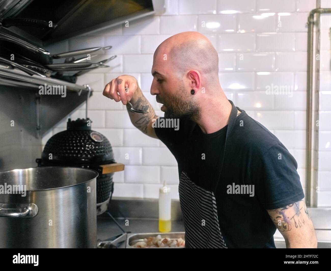 Lo chef assaggia il cibo da una pentola mentre lavora in una cucina del ristorante Foto Stock