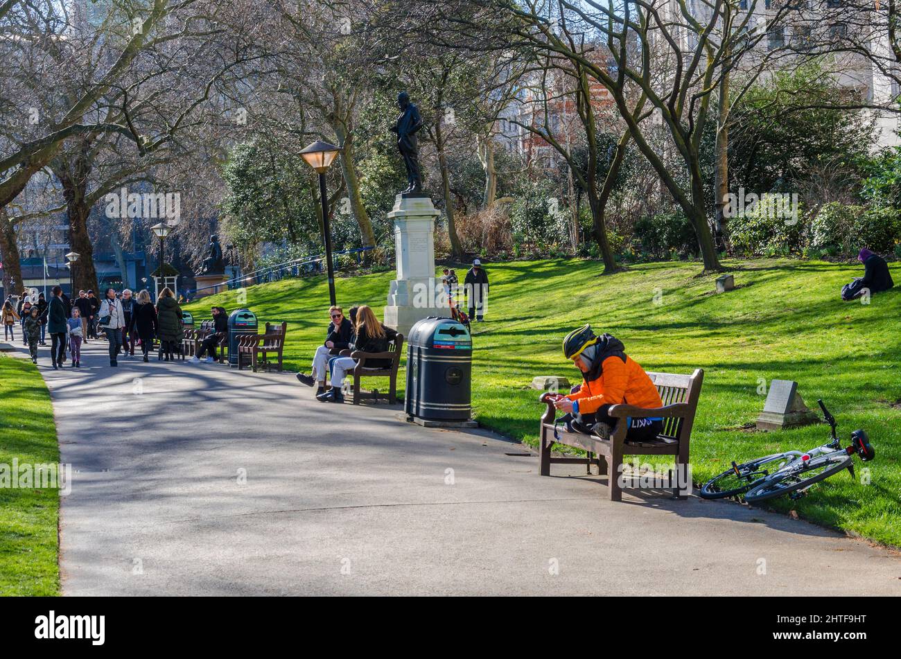 I London Memorial Gardens sono occupati di persone che camminano e si siedono su panchine lungo il percorso principale attraverso il parco. Foto Stock