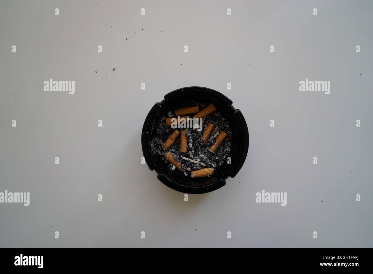Vista dall'alto di sigarette fumate in un posacenere nero su una superficie bianca Foto Stock