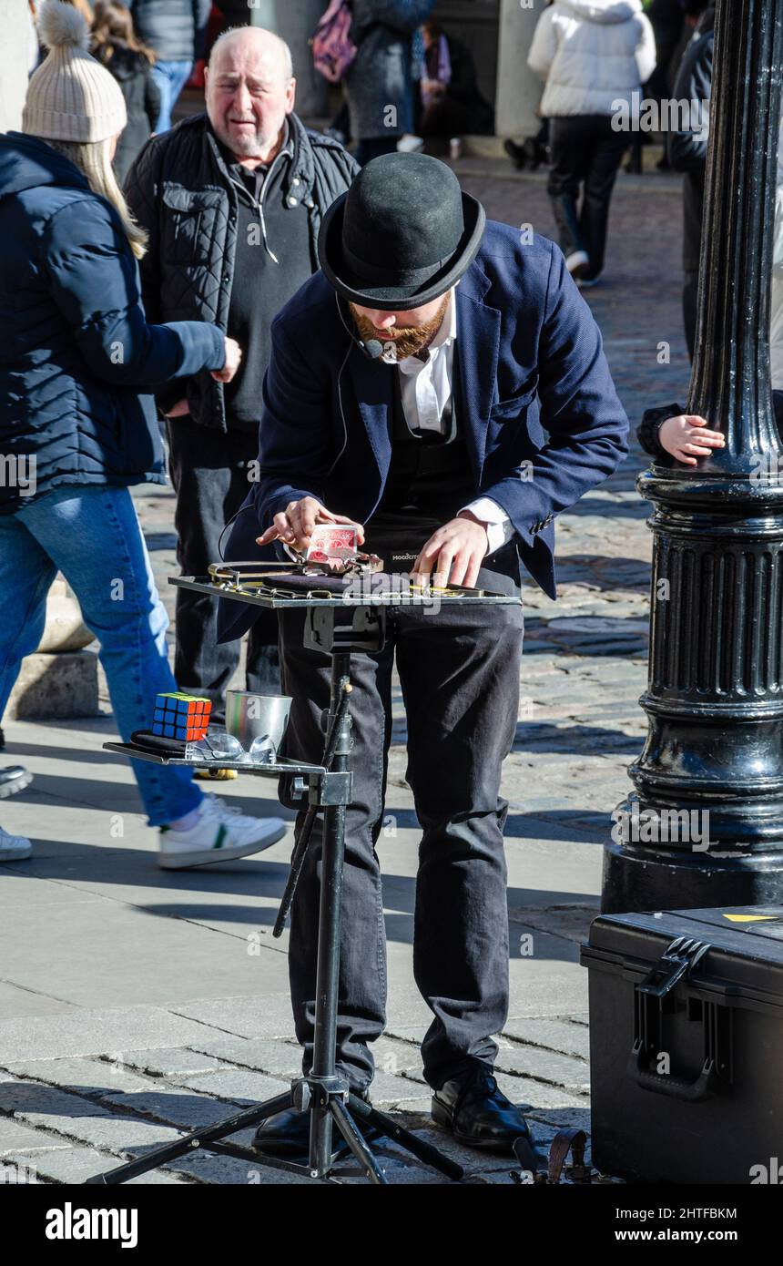 Un artista di strada che indossa un cappello da bowler che fa un trucco card per intrattenere una folla a Covent Garden a Londra, Regno Unito Foto Stock