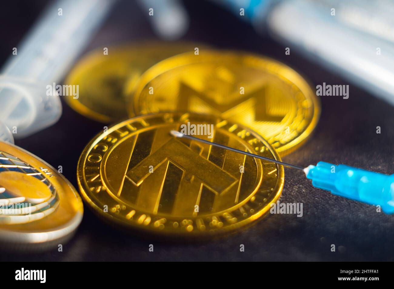 Primo piano di una moneta digitale tra una serie di siringhe Foto Stock