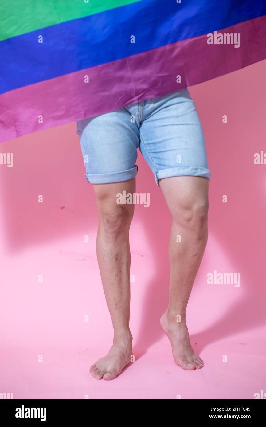 Metà di un giovane messicano che posa con bandiera LGBT su sfondo rosa Foto Stock