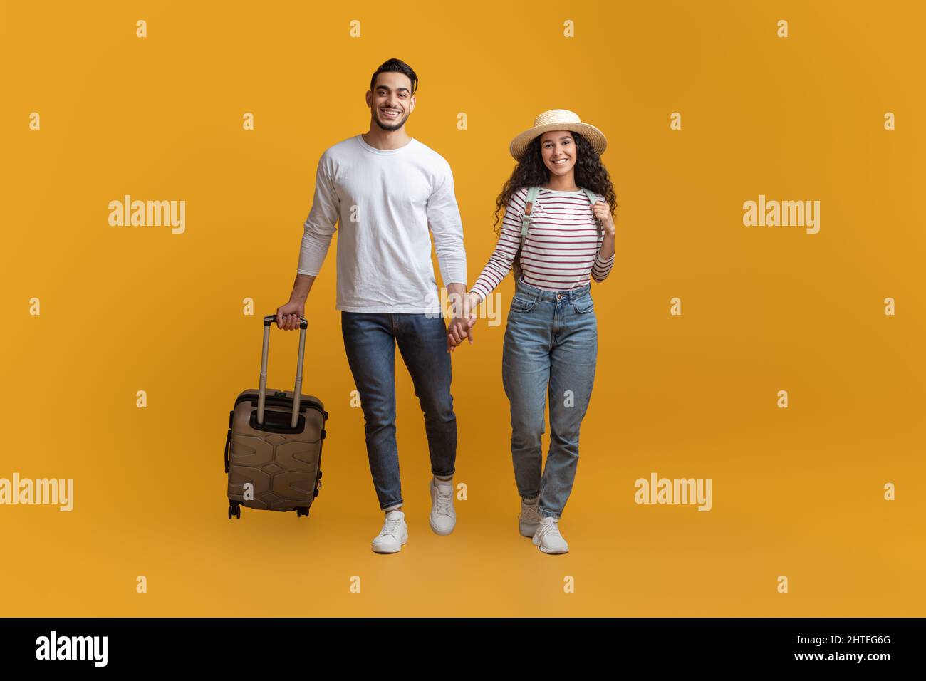 Tempo di vacanza. Giovane coppia Medio Oriente a piedi con bagaglio su sfondo giallo Foto Stock