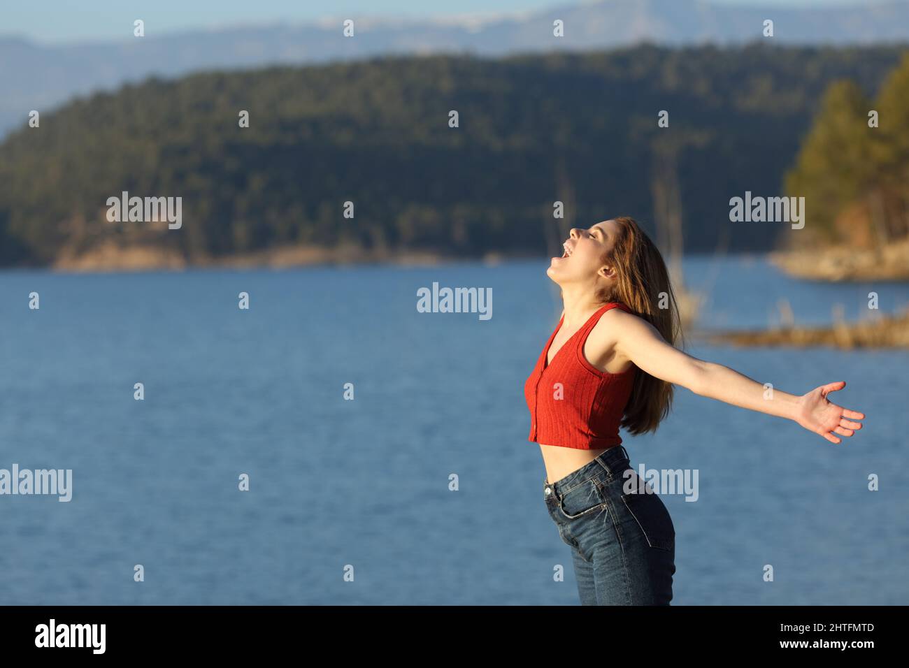 Profilo di una donna eccitata in rosso urlando braccia estenuanti in un lago Foto Stock