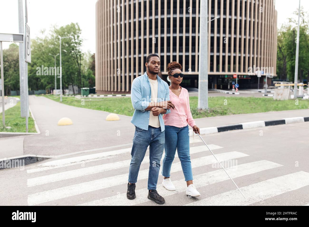 Donna millenaria afroamericana con disabilità visiva che attraversa la strada della città con il suo ragazzo o caregiver, spazio copia Foto Stock