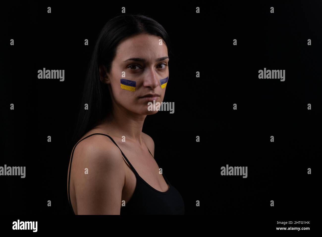 Ritratto di donna ucraina seria con bandiera ucraina blu e gialla sulla guancia. Il simbolo dell'inviolabilità del popolo ucraino. Scuri ba Foto Stock