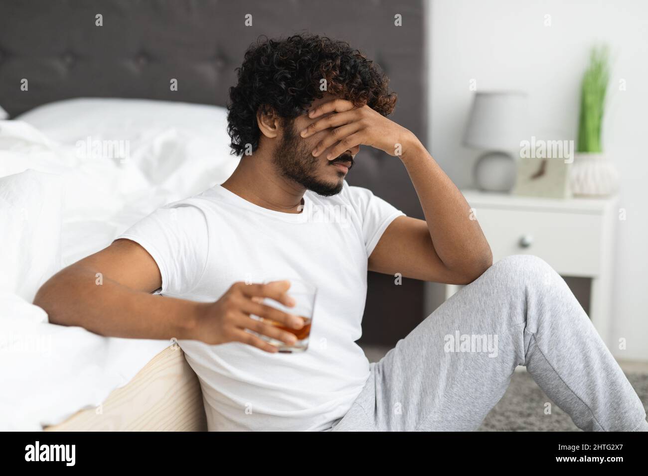 Uomo indiano depresso che beve alcol, seduto a letto da pavimento Foto Stock