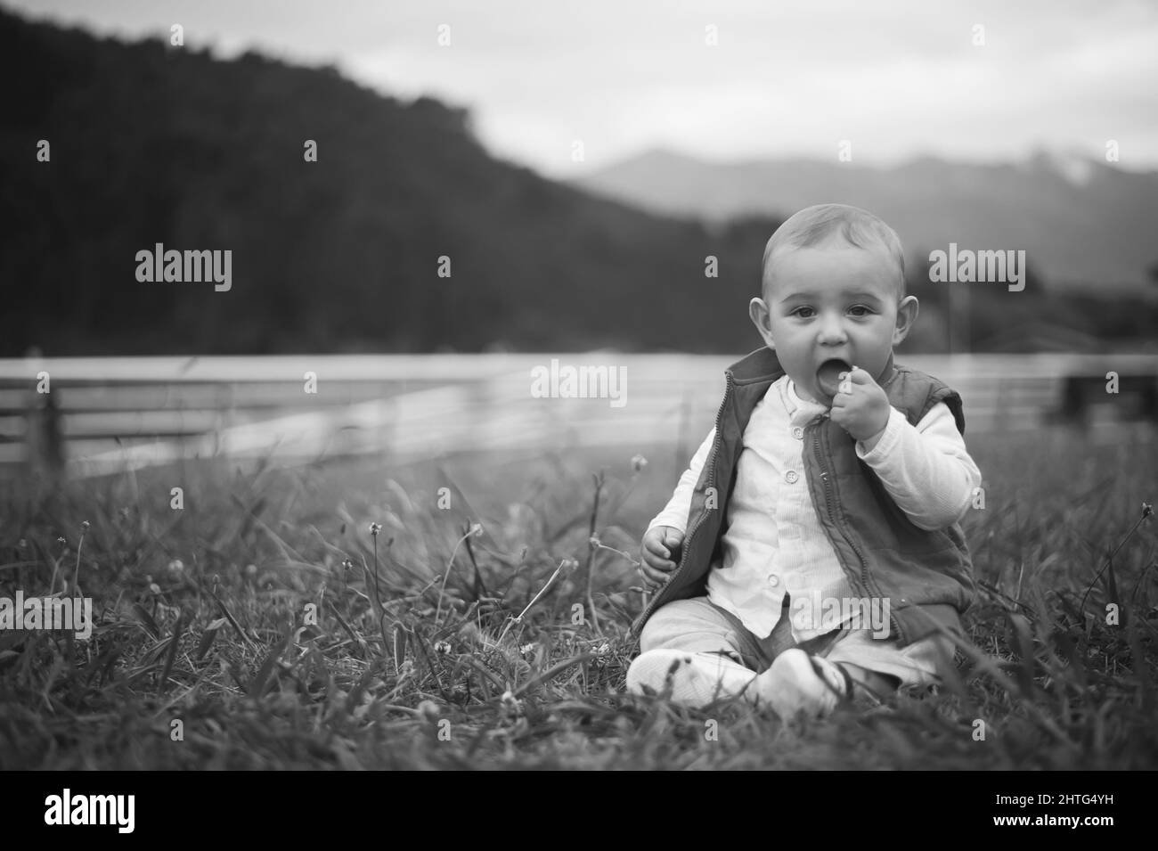 Primo piano di un bambino caucasico seduto sull'erba in bianco e nero Foto Stock