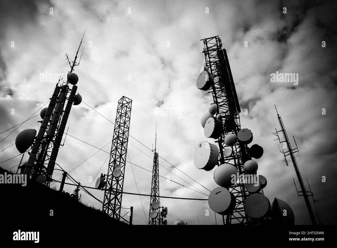 Immagine inferiore in scala di grigi delle antenne radio sullo sfondo delle nuvole. Foto Stock