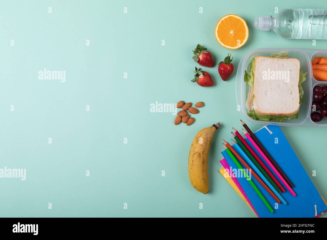 Frutta con sandwich in scatola tiffin bottiglia d'acqua, matite colorate e libri su sfondo verde Foto Stock