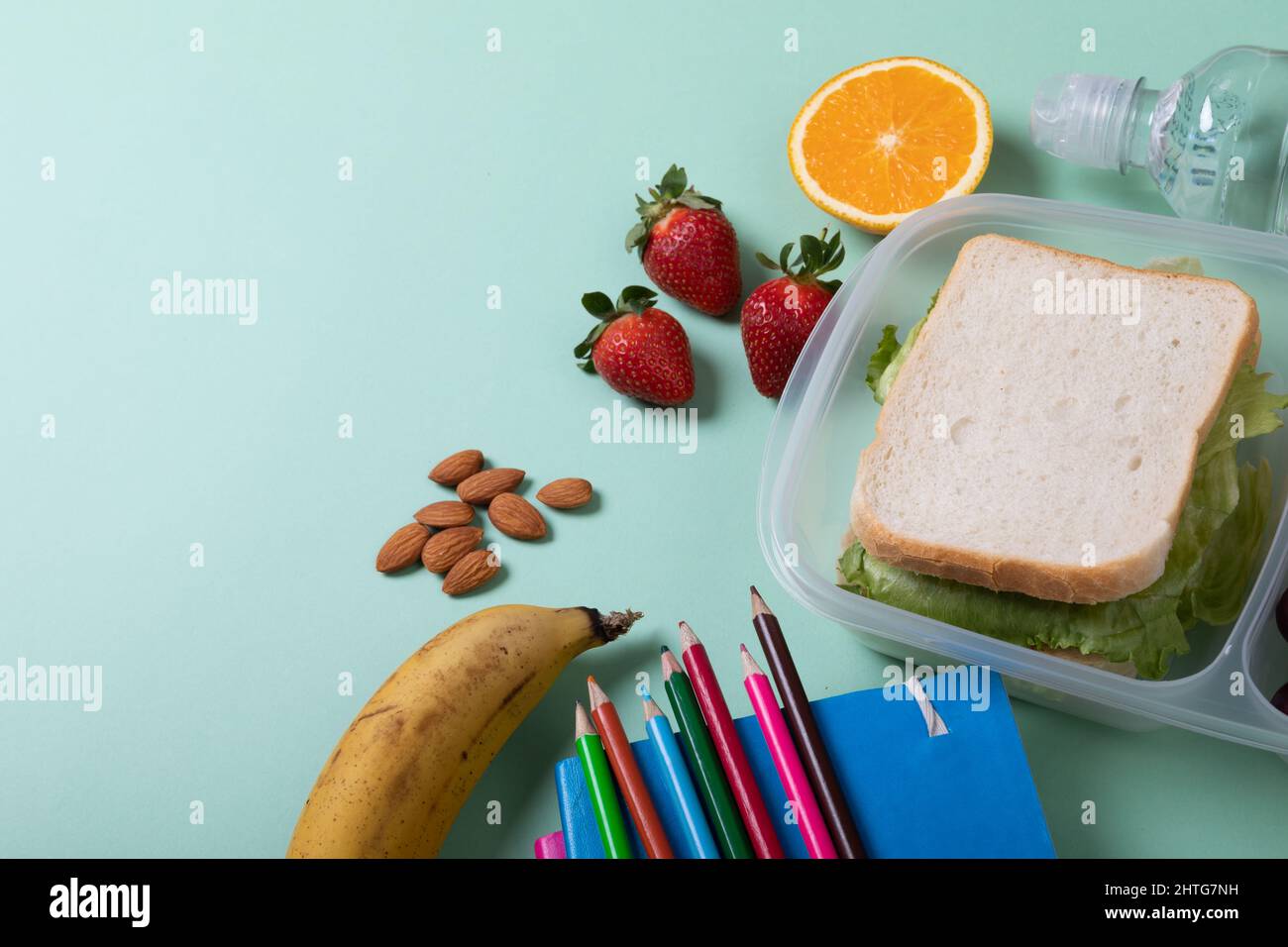 Sandwich nel pranzo al sacco con frutta, mandorle e matite colorate con libri su sfondo verde Foto Stock