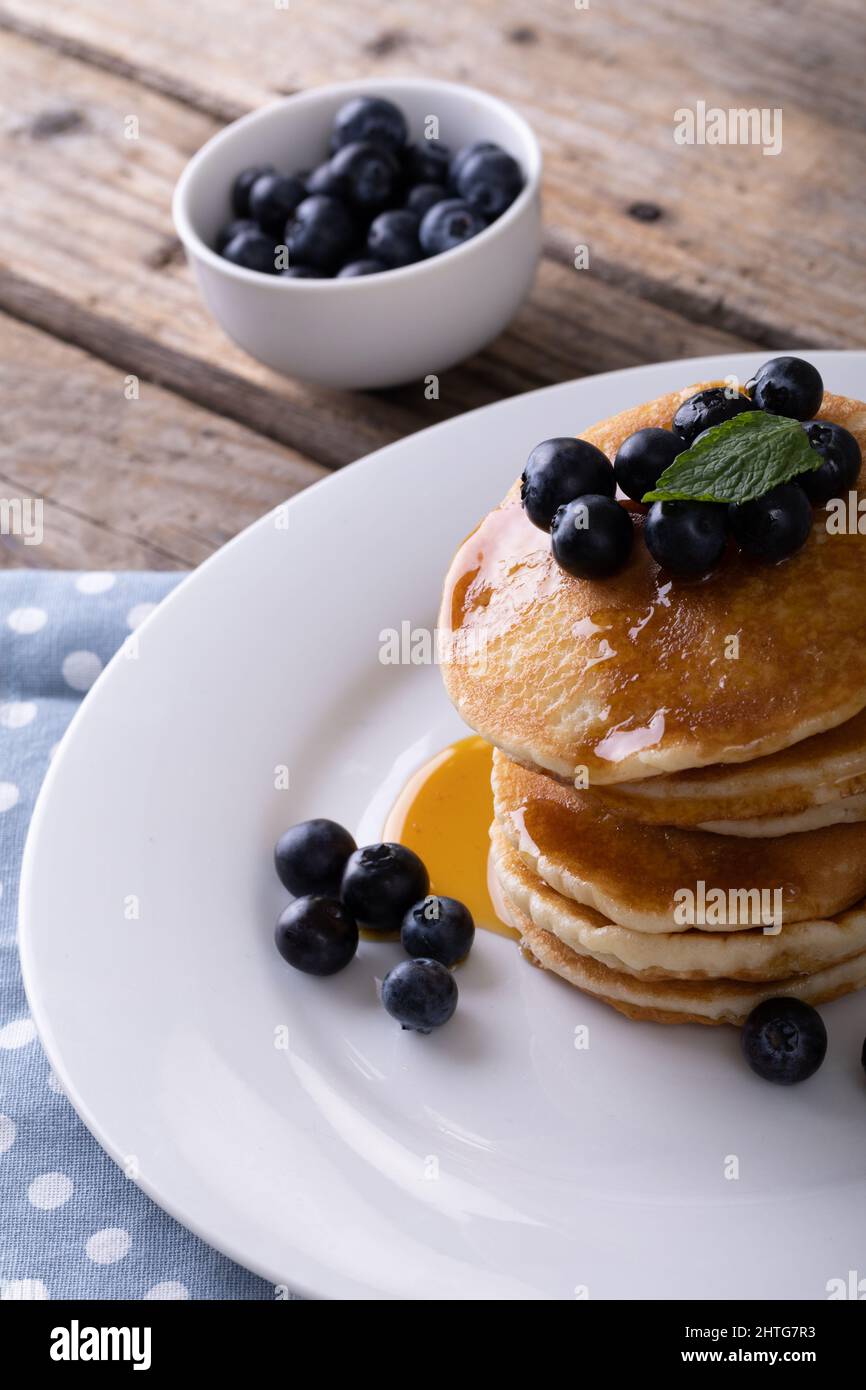 Primo piano di frittelle appetitose con sciroppo, erbe e mirtilli serviti in piatto sul tavolo Foto Stock