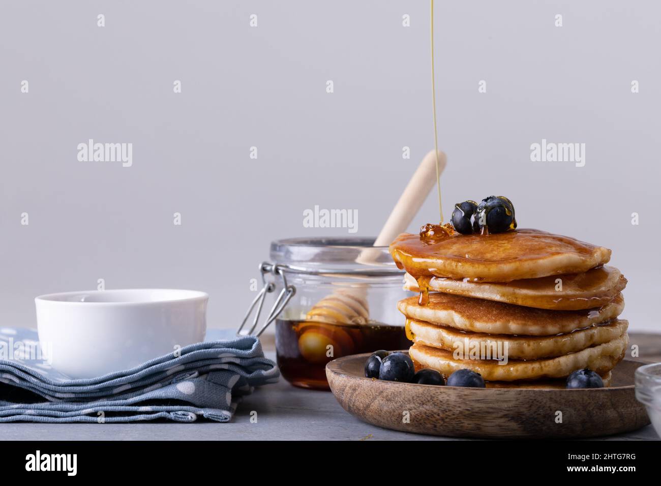 Primo piano di frittelle accatastate con bacche blu e miele gocciolante su sfondo grigio Foto Stock