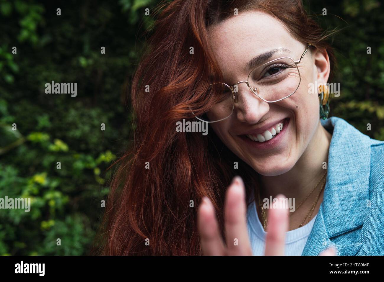 Ritratto di donna sorridente con lunghi capelli rossi che tirano la mano verso la fotocamera. Ritratto di bellezza di donna naturale divertirsi Foto Stock