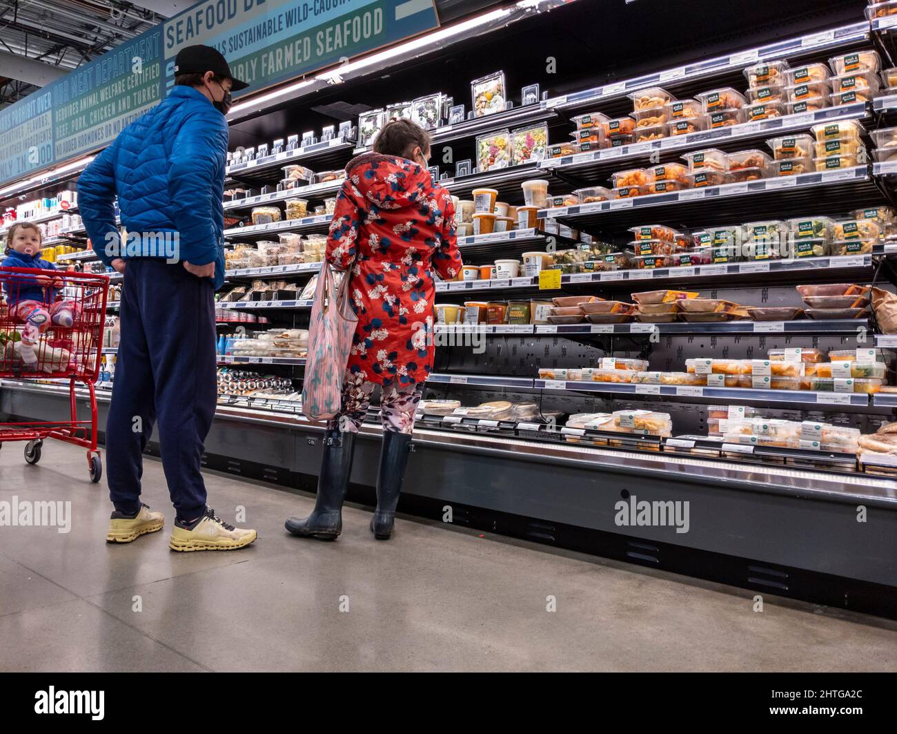 Kirkland, WA USA - circa Febbraio 2022: Vista di un uomo e una donna con il loro bambino, shopping al corridoio di cibo preparato all'interno di un intero mercato di cibi Foto Stock Kirkland, WA USA - circa Febbraio 2022: Vista di un uomo e una donna con il loro bambino, shopping al corridoio di cibo preparato all'interno di un intero mercato di cibi Foto Stock