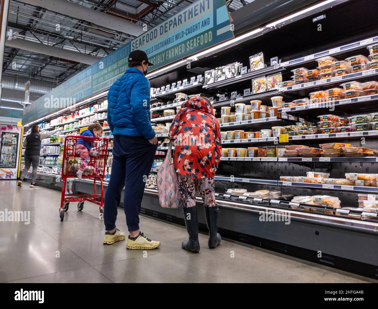 Kirkland, WA USA - circa Febbraio 2022: Vista di un uomo e una donna con il loro bambino, shopping al corridoio di cibo preparato all'interno di un intero mercato di cibi. Foto Stock Kirkland, WA USA - circa Febbraio 2022: Vista di un uomo e una donna con il loro bambino, shopping al corridoio di cibo preparato all'interno di un intero mercato di cibi. Foto Stock