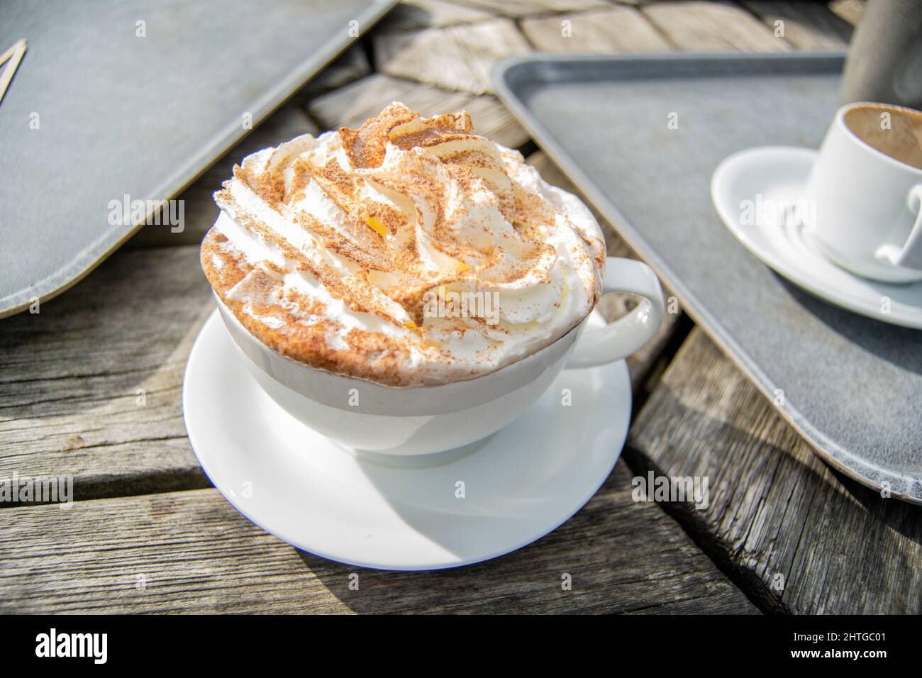 Primo piano per una grande tazza bianca di cioccolata calda con panna montata e spruzzi di cacao sulla parte superiore, tazza con bevanda standig sul tavolo esterno in legno accanto a. Foto Stock Primo piano per una grande tazza bianca di cioccolata calda con panna montata e spruzzi di cacao sulla parte superiore, tazza con bevanda standig sul tavolo esterno in legno accanto a. Foto Stock