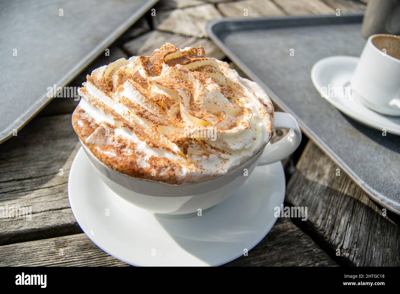 Primo piano per una grande tazza bianca di cioccolata calda con panna montata e spruzzi di cacao sulla parte superiore, tazza con bevanda standig sul tavolo esterno in legno accanto a. Foto Stock Primo piano per una grande tazza bianca di cioccolata calda con panna montata e spruzzi di cacao sulla parte superiore, tazza con bevanda standig sul tavolo esterno in legno accanto a. Foto Stock