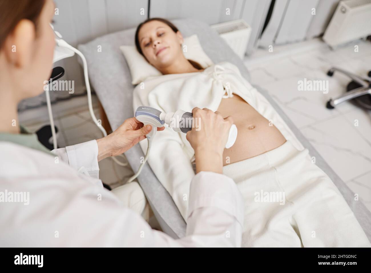 Primo piano di una dottoressa che mette il gel sul trasduttore a ultrasuoni mentre esamina la giovane donna incinta in clinica, spazio copia Foto Stock