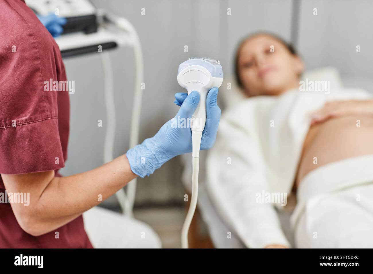 Primo piano di una dottore che tiene il trasduttore a ultrasuoni durante l'esame di una giovane donna incinta in clinica, spazio copia Foto Stock