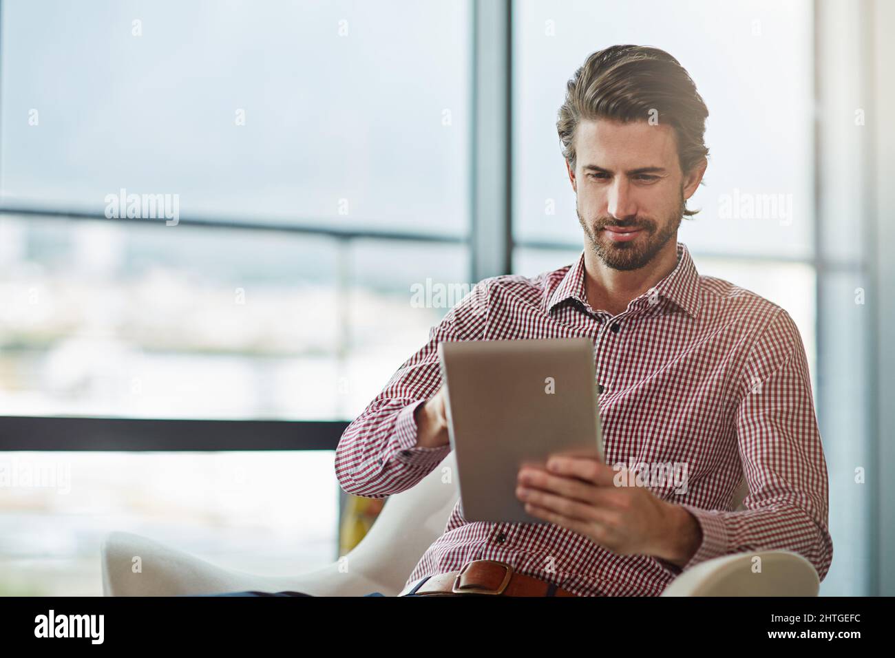 Il suo tablet gli consente di lavorare ovunque. Scatto di un bel giovane uomo d'affari usando il suo tablet in ufficio. Foto Stock