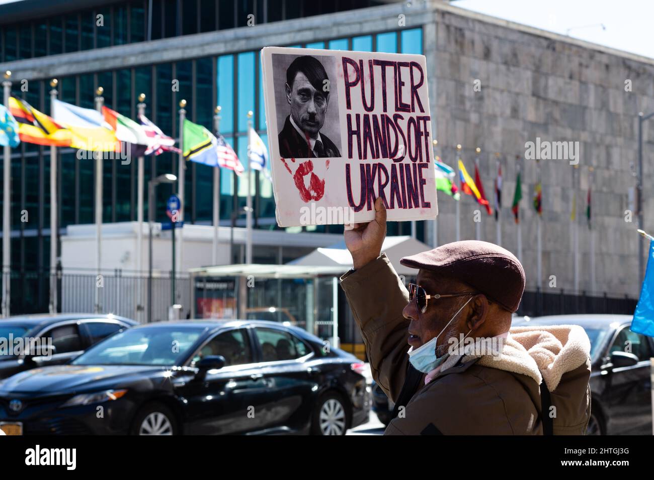 New York, NY, USA. 28th Feb 2022. I manifestanti pro-ucraini si trovano di fronte alle Nazioni Unite dall'altra parte della First Avenue. Un uomo porta un segno con una foto di Putin con un taglio di capelli e baffi come Adolf Hitler, e che dice “Putler [sic.] Mani fuori l'Ucraina." Credit: Ed Lefkowicz/Alamy Live News Foto Stock