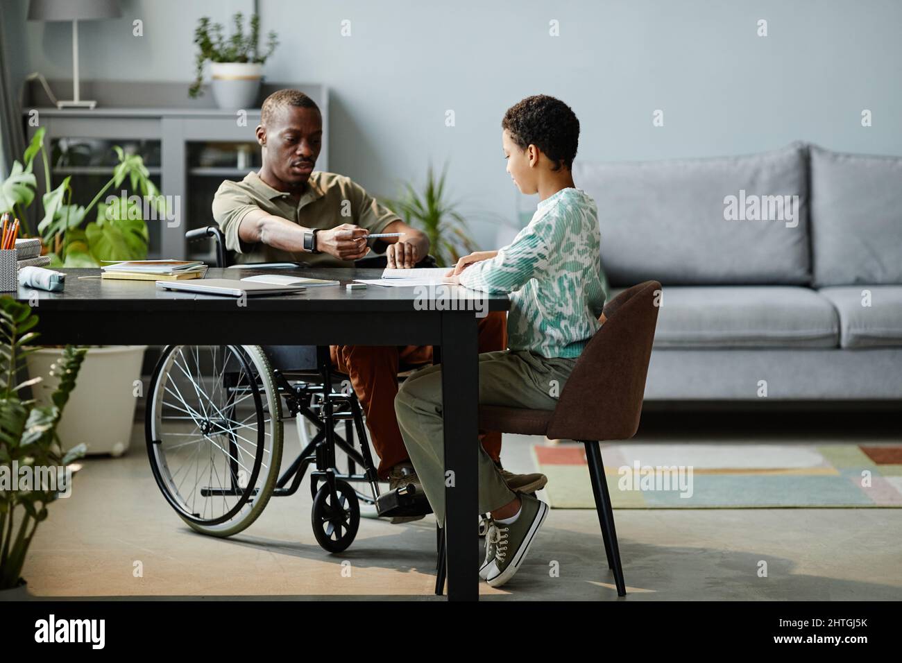 Ritratto completo di padre con disabilità aiutare figlia a studiare a casa, spazio copia Foto Stock