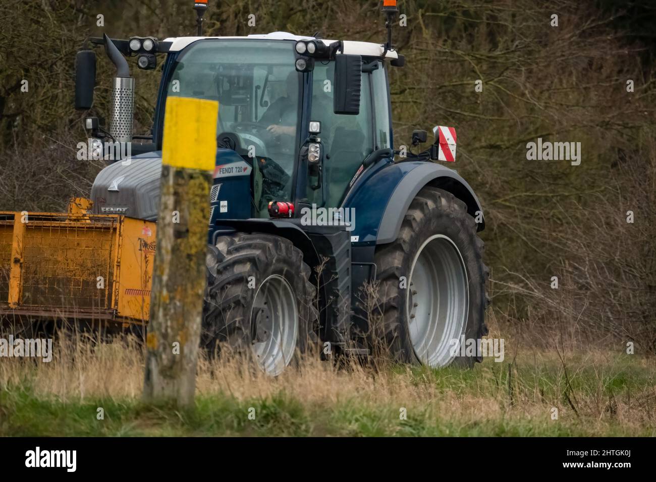 Trattore FENDT 720 dotato di una scatola di trasporto con attacco rapido Twose gialla, che procede lungo una corsia di campagna Foto Stock