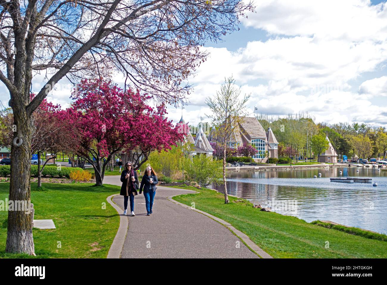 Due donne che si godono una passeggiata intorno al lago Harriet sotto alberi da frutto fiorenti. Minneapolis Minnesota, Stati Uniti Foto Stock