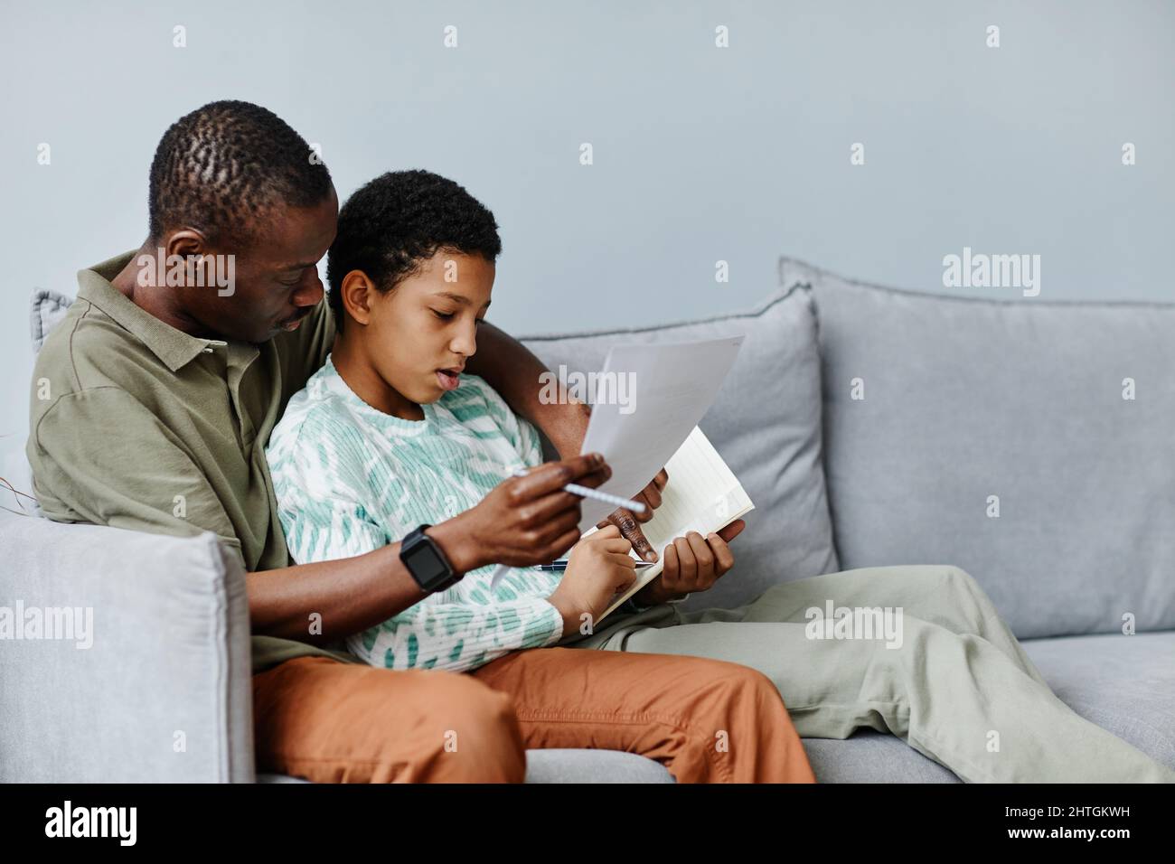 Ritratto con vista laterale minima di un uomo afro-americano che aiuta la figlia a fare i compiti mentre si siede sul divano a casa, spazio copia Foto Stock