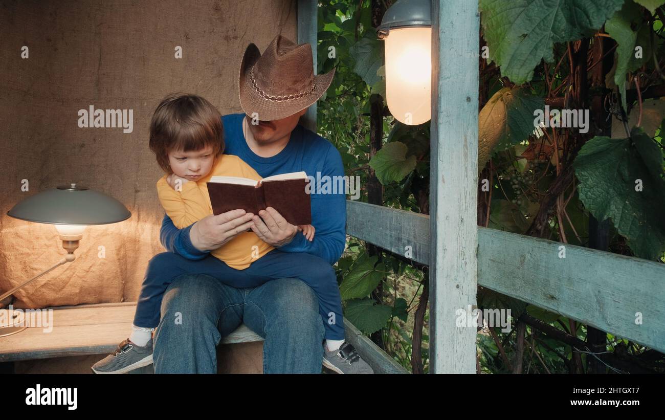 L'uomo in cappello cowboy legge libro di carta a bambino seduto sul portico  della casa del villaggio Foto stock - Alamy