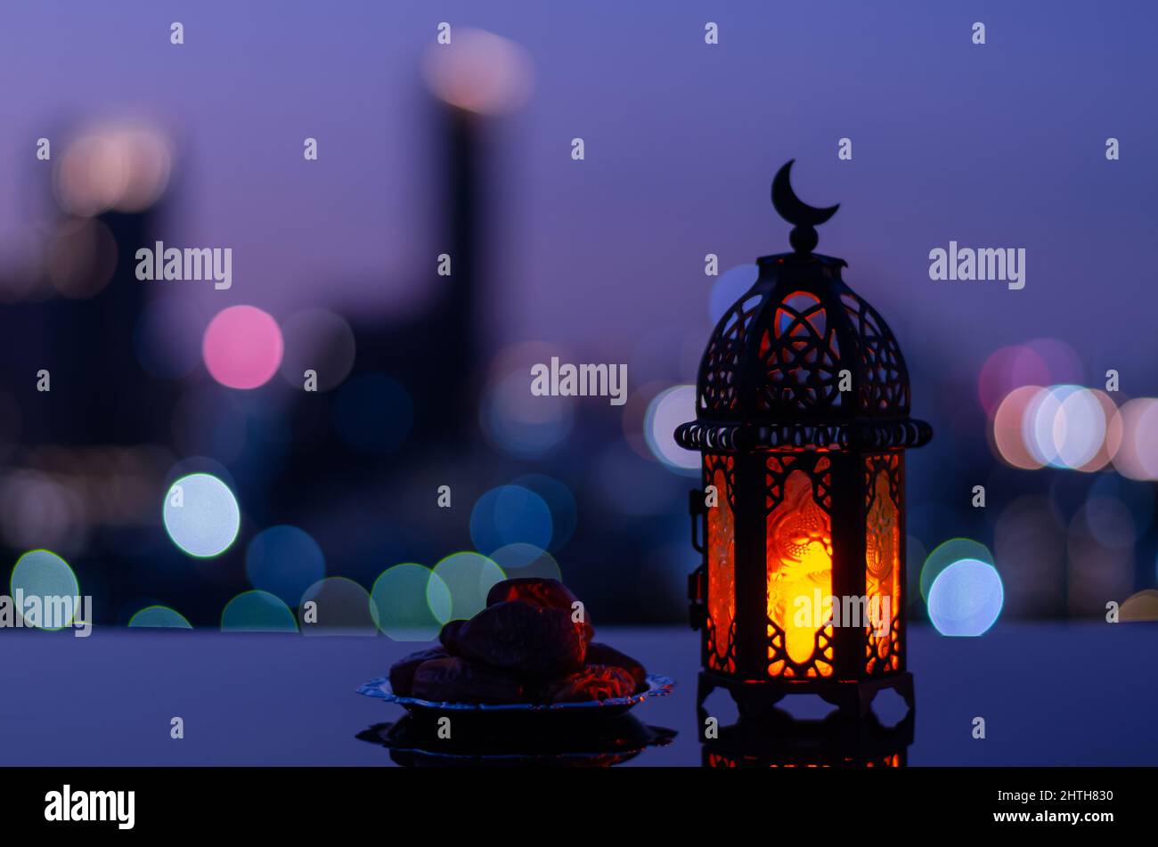 Fuoco selettivo di lanterna che hanno simbolo di luna sulla parte superiore e piccolo piatto di datteri frutto con bokeh città sfondo chiaro per la festa musulmana del ho Foto Stock