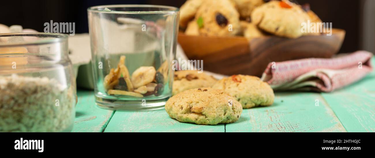 Cottura di biscotti di farina d'avena con frutta candita e noci. Uova, farinata d'avena, farina, zucchero, spezie e utensili da cucina su un vecchio legno Foto Stock