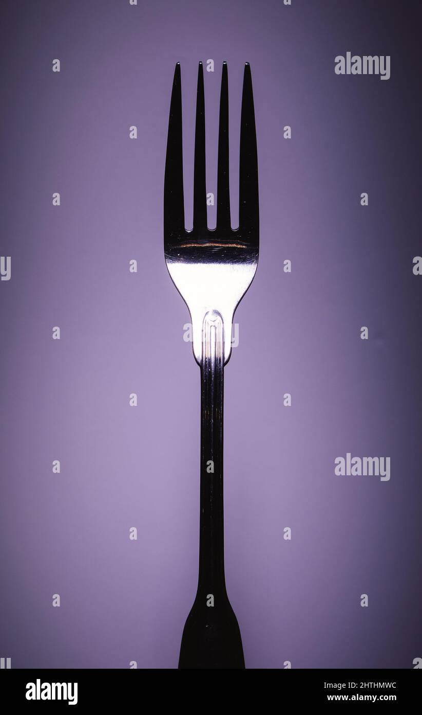 Primo piano di una forchetta metallica su sfondo viola, approccio minimalista, composizione studio. Foto Stock