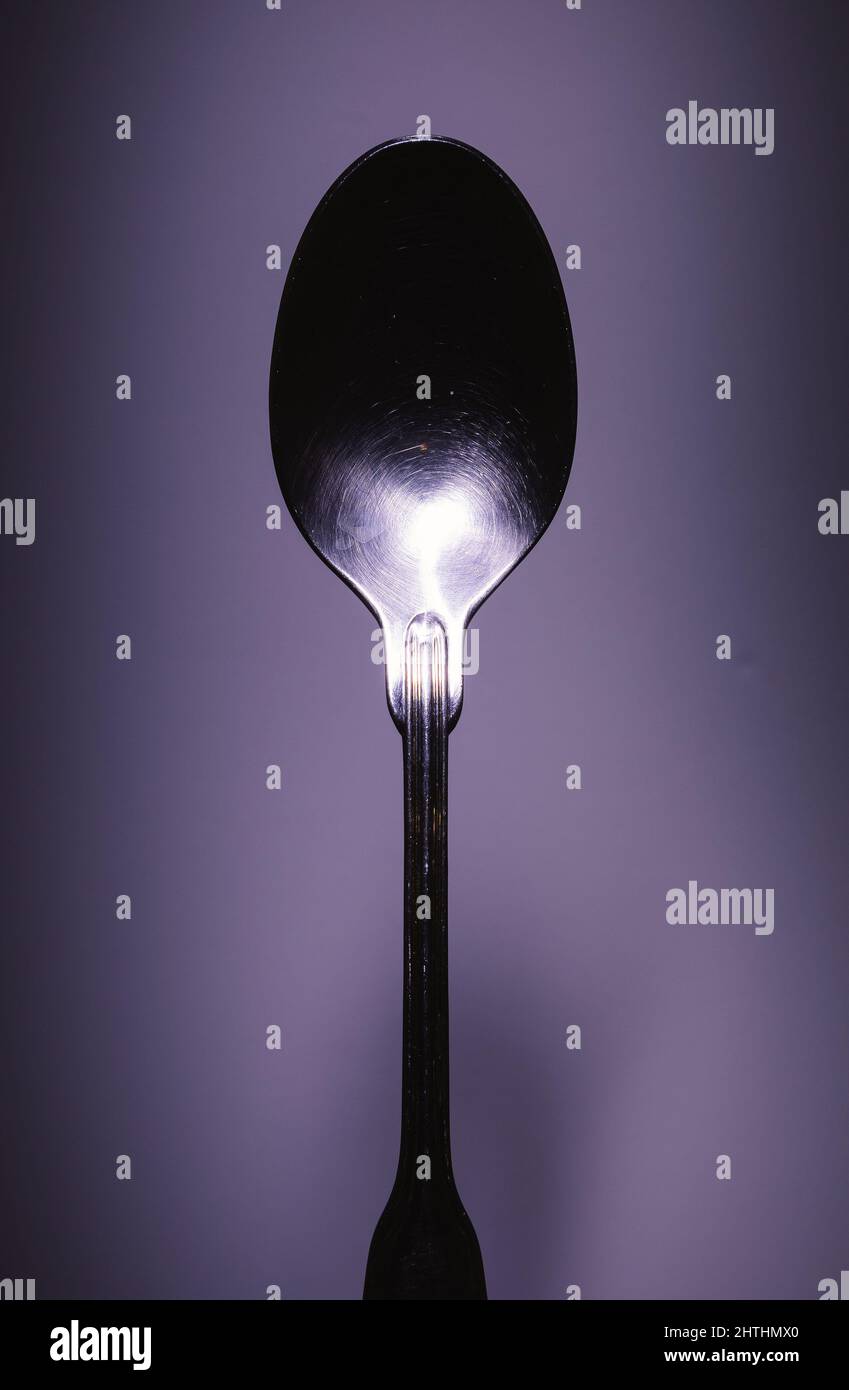 Primo piano di un cucchiaio di metallo su sfondo viola, approccio minimalista, composizione studio. Foto Stock