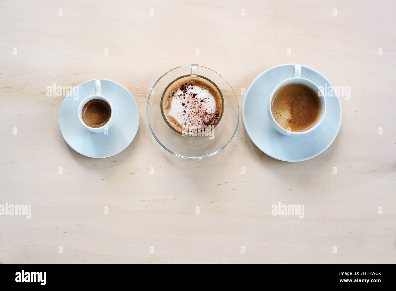 Tre tazze con vari tipi di caffè, espresso, cappuccino e crema lungo su un tavolo di legno chiaro, spazio copia, vista dall'alto, messa a fuoco selezionata Foto Stock