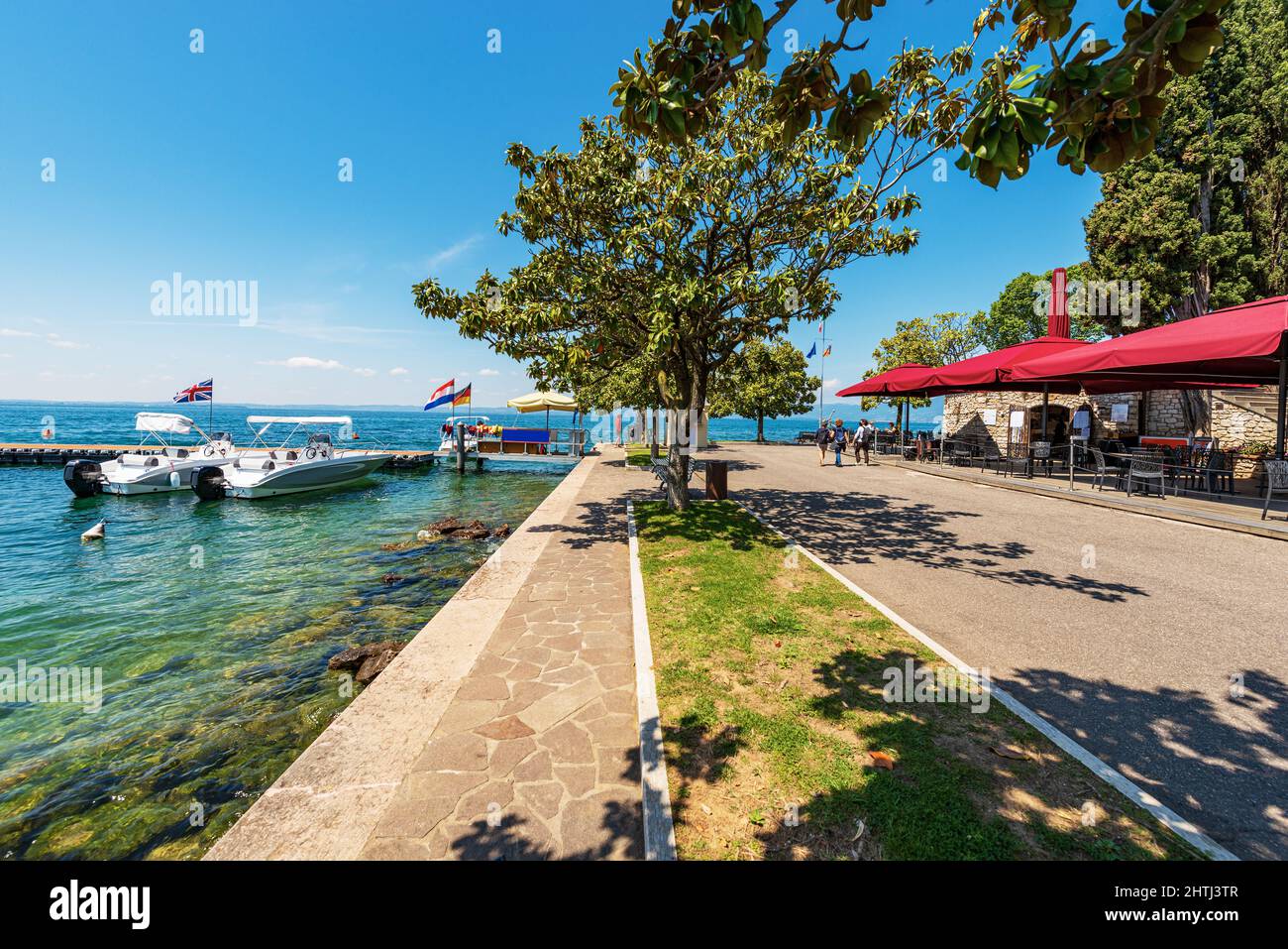 Passeggiata sul lago di Garda con molo in legno e due motoscafi. Piccolo borgo di Bardolino, località turistica, Verona, Veneto, Italia Foto Stock