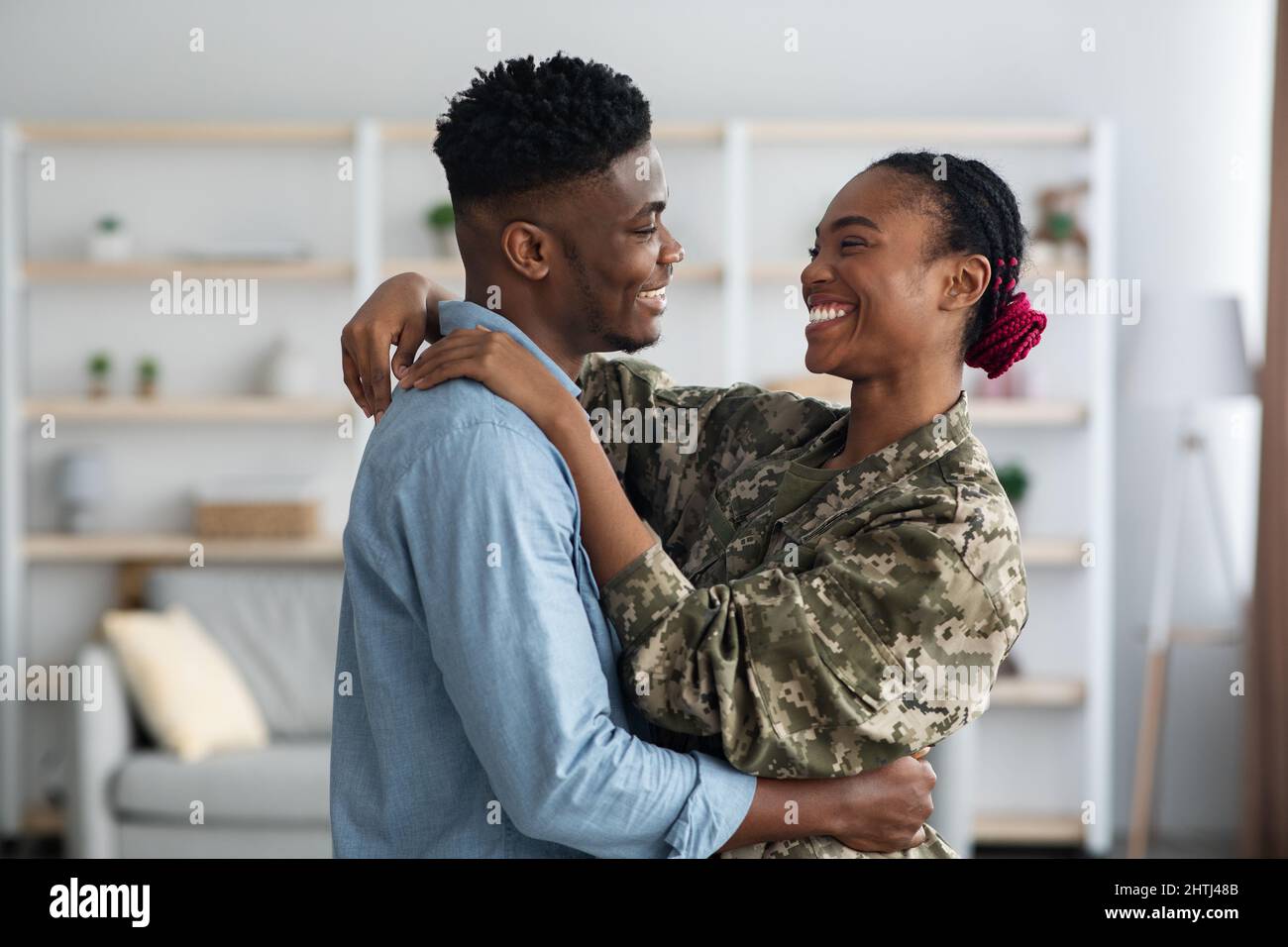 Famiglia nera amorevole moglie e marito militare abbracciare a casa Foto Stock