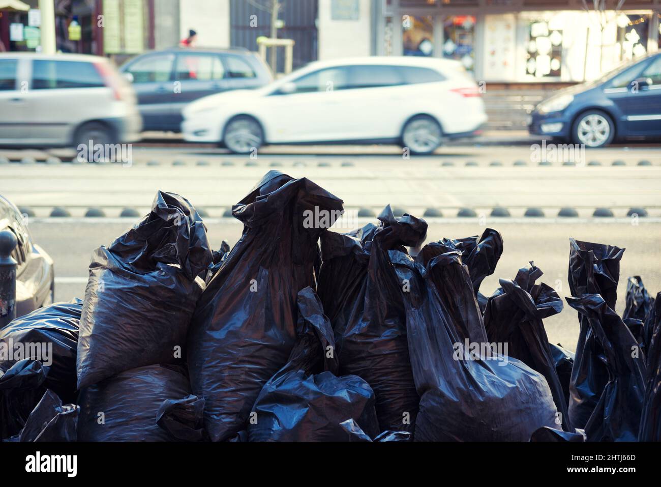 Via della città. Sacchi di rifiuti neri impilati su un lato guida Foto Stock