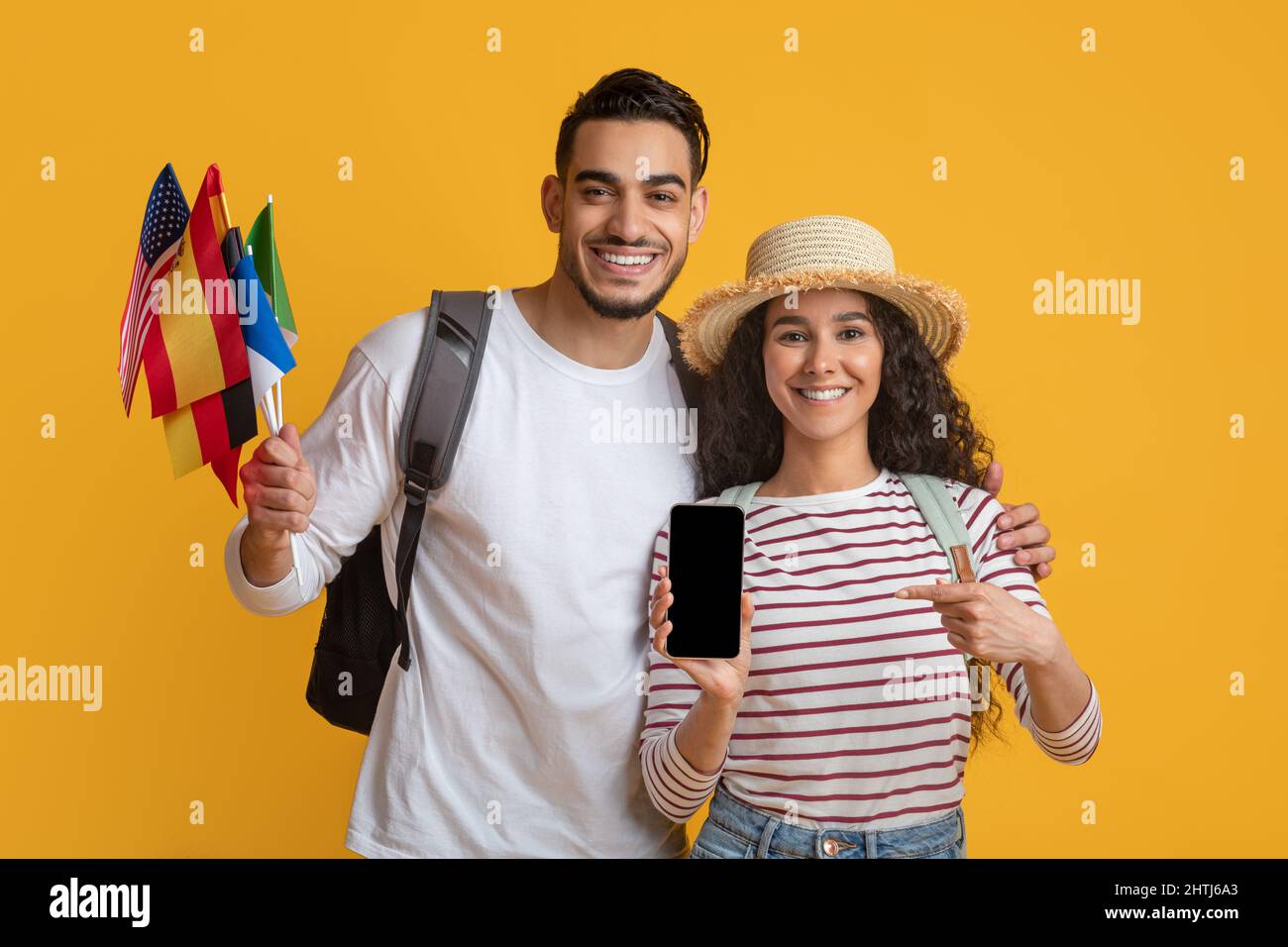 App per traduttori online. Happy Young Couple Holding International Flags e smartphone in bianco Foto Stock