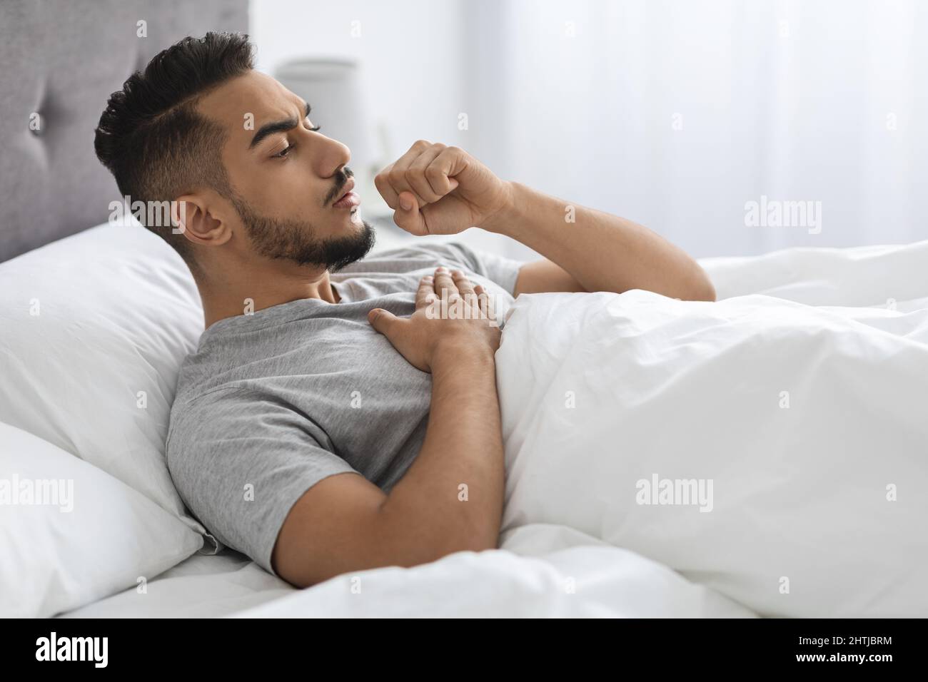 Malata giovane arabo uomo tosse mentre sdraiato a letto a casa Foto Stock